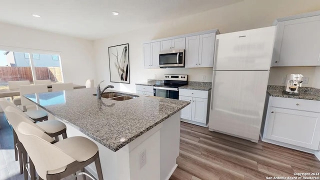 kitchen featuring light stone counters, wood finished floors, a sink, appliances with stainless steel finishes, and a kitchen bar