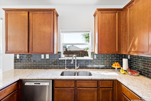 kitchen featuring light stone counters, brown cabinetry, a sink, stainless steel dishwasher, and backsplash