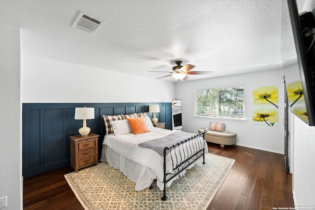 bedroom featuring visible vents, ceiling fan, wainscoting, a textured ceiling, and dark wood-style flooring