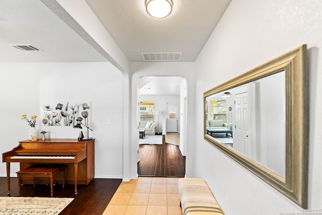 corridor featuring arched walkways, visible vents, baseboards, and hardwood / wood-style flooring