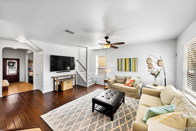 living area featuring visible vents, ceiling fan, dark wood finished floors, arched walkways, and a textured ceiling