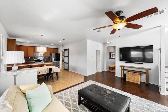 living room with visible vents, a barn door, wood-type flooring, and ceiling fan