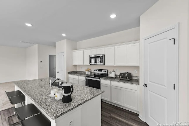 kitchen with light stone counters, dark wood finished floors, a kitchen island with sink, stainless steel appliances, and white cabinets