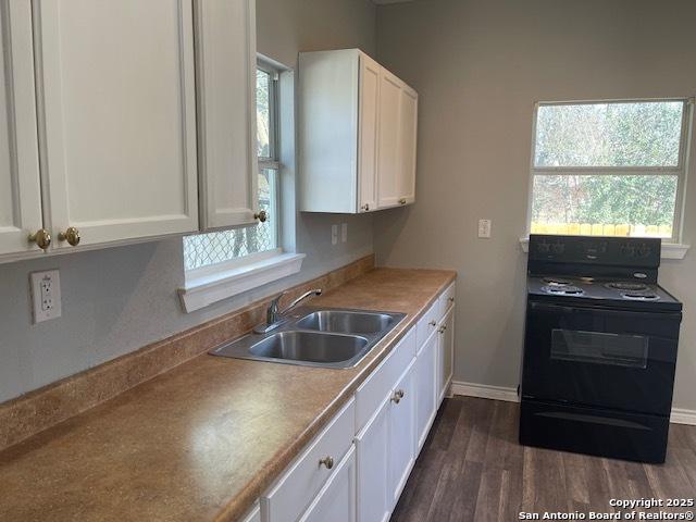 kitchen with dark wood-type flooring, a sink, black / electric stove, white cabinets, and baseboards