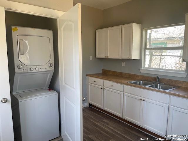 clothes washing area featuring laundry area, stacked washer / dryer, dark wood-style floors, and a sink