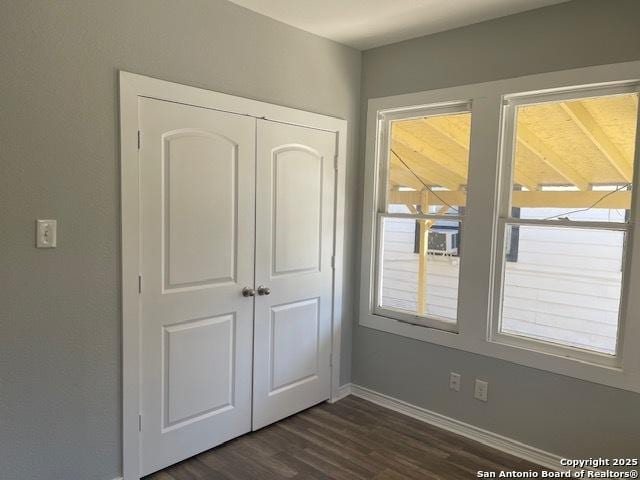 unfurnished bedroom featuring baseboards, a closet, and dark wood-style flooring