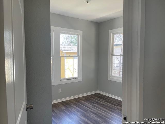 empty room featuring a wealth of natural light, baseboards, and dark wood-style floors