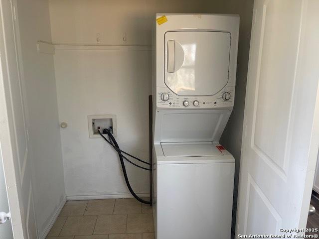 washroom with light tile patterned floors, baseboards, and stacked washing maching and dryer