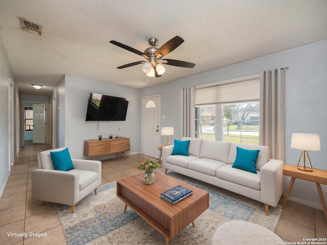 living room featuring light tile patterned floors, baseboards, visible vents, ceiling fan, and a textured ceiling