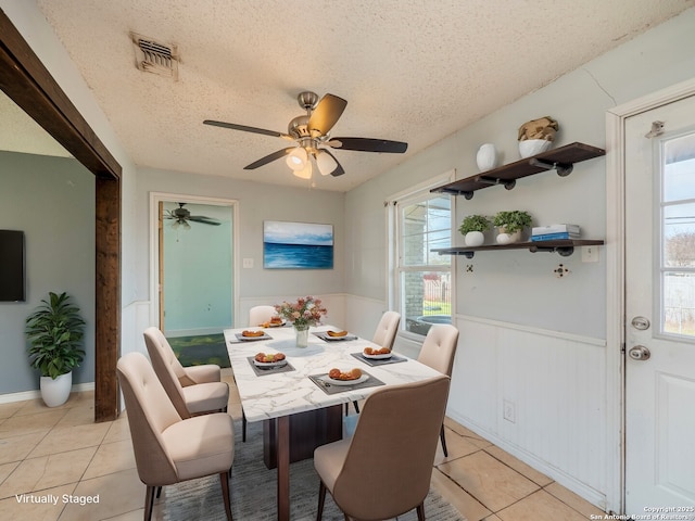 dining room with visible vents, ceiling fan, a wainscoted wall, light tile patterned floors, and a textured ceiling