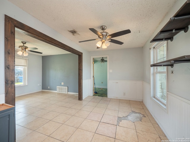 spare room featuring light tile patterned flooring, wainscoting, visible vents, and ceiling fan