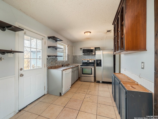 kitchen with light tile patterned floors, open shelves, a sink, appliances with stainless steel finishes, and tasteful backsplash