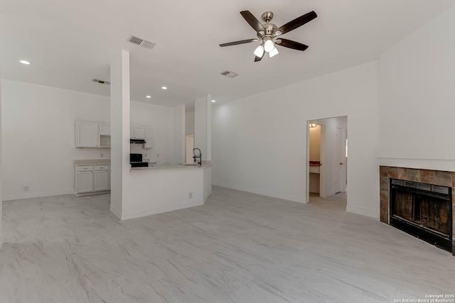 unfurnished living room with a sink, visible vents, a ceiling fan, and a tile fireplace