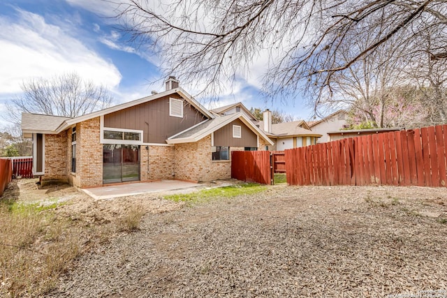 back of house featuring a patio, fence private yard, brick siding, and a chimney