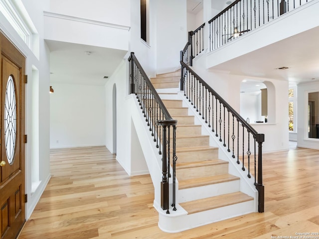 entrance foyer with arched walkways, plenty of natural light, a towering ceiling, and wood finished floors