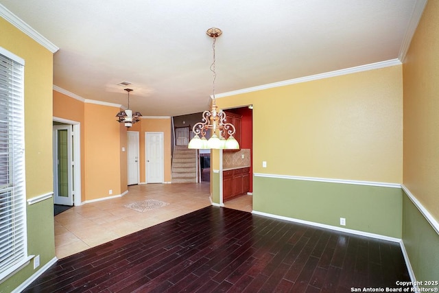 empty room featuring a notable chandelier, ornamental molding, baseboards, and wood finished floors