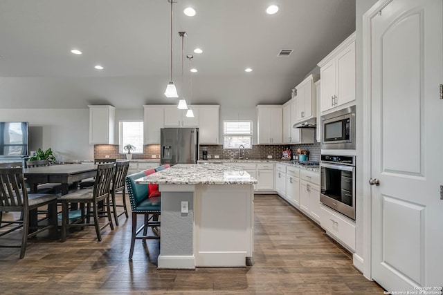 kitchen with visible vents, a sink, a kitchen island, stainless steel appliances, and decorative backsplash