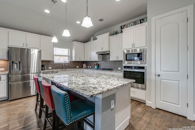 kitchen with visible vents, a kitchen island, appliances with stainless steel finishes, wood finished floors, and white cabinetry