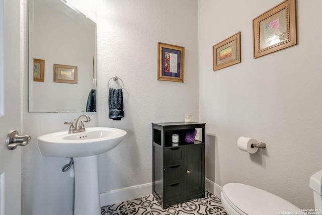 bathroom featuring toilet, baseboards, and a sink