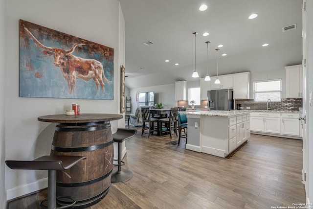 kitchen featuring a center island, decorative backsplash, stainless steel refrigerator with ice dispenser, wood finished floors, and white cabinetry