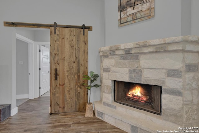 unfurnished living room featuring wood finished floors, visible vents, baseboards, a stone fireplace, and a barn door