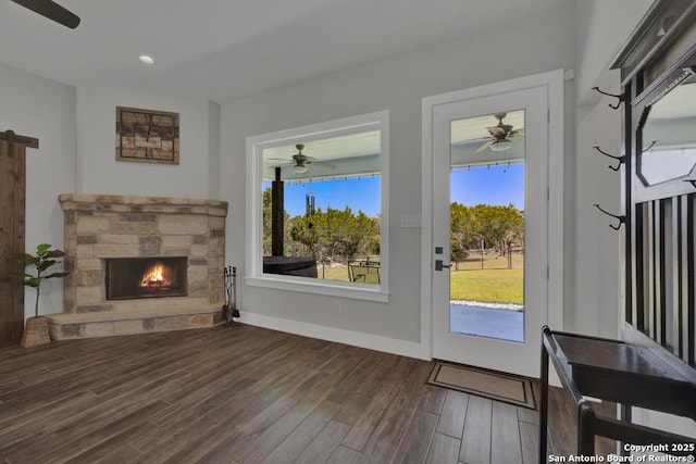 living room with wood finished floors, baseboards, ceiling fan, a stone fireplace, and a barn door