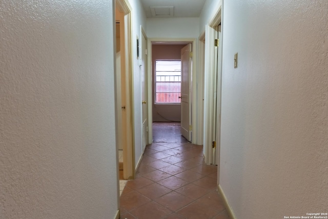 corridor with tile patterned floors, a textured wall, and baseboards