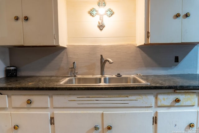 kitchen featuring white cabinetry, dark countertops, decorative backsplash, and a sink