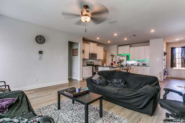 living room featuring visible vents, baseboards, a ceiling fan, and light wood finished floors