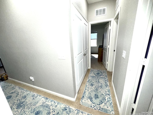 hall with visible vents, baseboards, and a textured wall