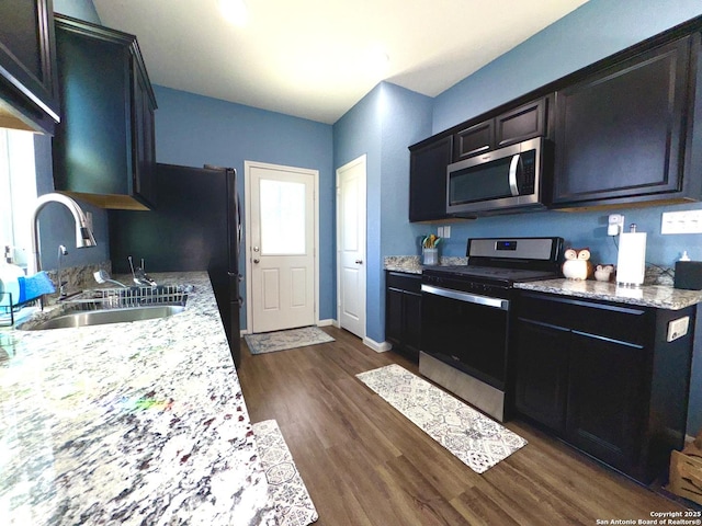 kitchen with a sink, baseboards, appliances with stainless steel finishes, dark wood-style floors, and dark cabinets