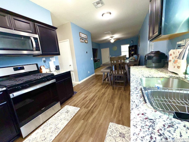 kitchen featuring baseboards, visible vents, light wood finished floors, stainless steel appliances, and dark brown cabinetry