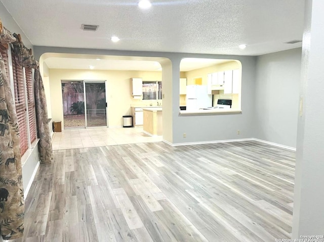 unfurnished living room with visible vents, a textured ceiling, and light wood finished floors