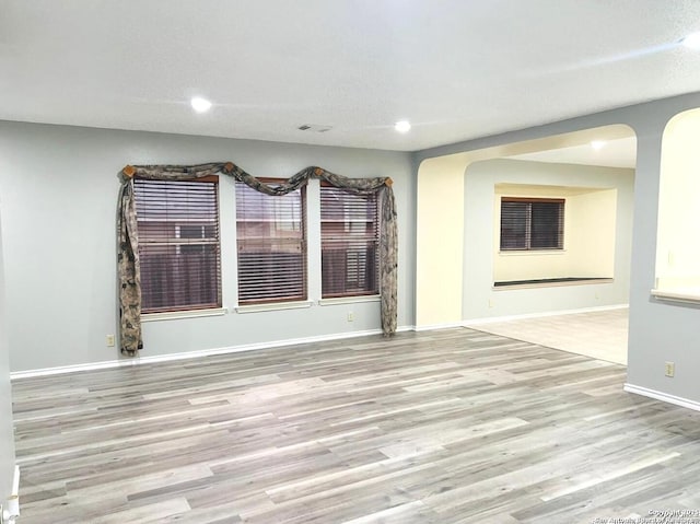 empty room with recessed lighting, baseboards, arched walkways, and wood finished floors