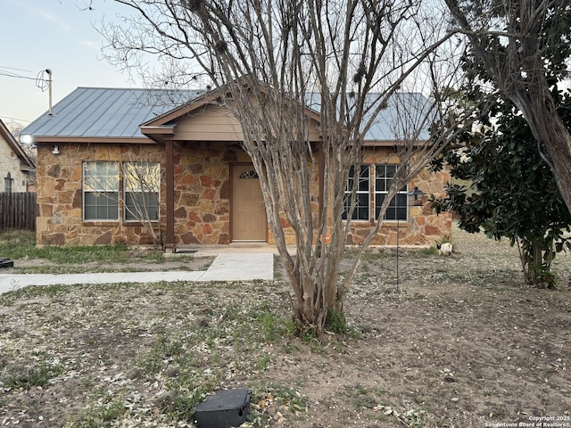 view of front of house with stone siding, metal roof, and fence