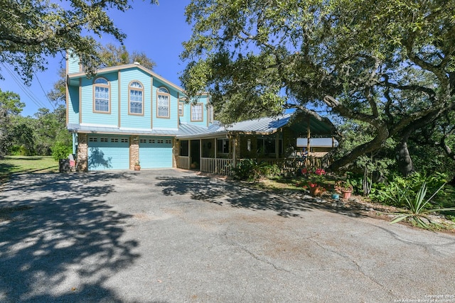 view of front of house featuring aphalt driveway, a porch, a chimney, and a garage