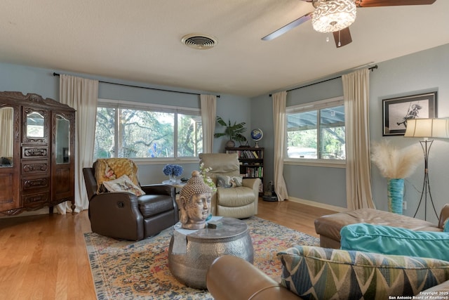 living room featuring visible vents, baseboards, wood finished floors, and a ceiling fan