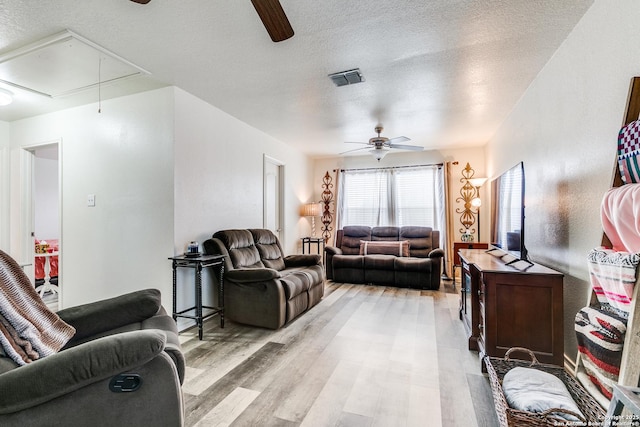 living room featuring light wood finished floors, visible vents, ceiling fan, attic access, and a textured ceiling