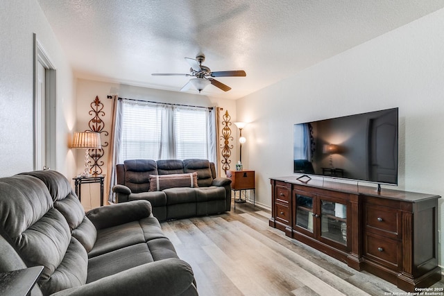 living area featuring baseboards, a textured ceiling, light wood-type flooring, and a ceiling fan