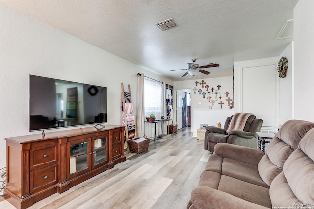 living room with light wood-style flooring, a ceiling fan, visible vents, and a textured ceiling