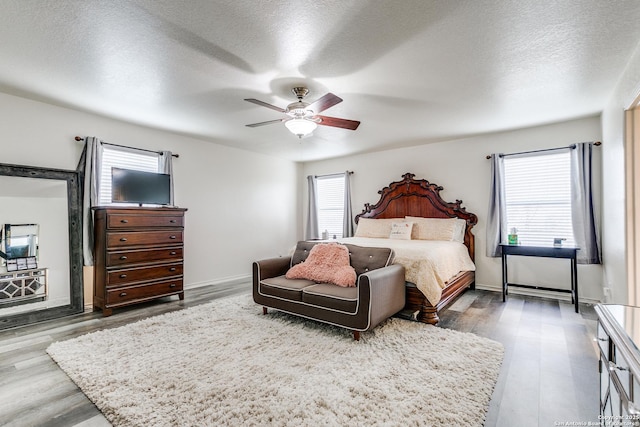 bedroom with a ceiling fan, wood finished floors, baseboards, and a textured ceiling