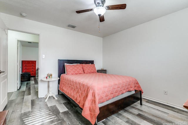 bedroom with ceiling fan, visible vents, baseboards, and wood finished floors