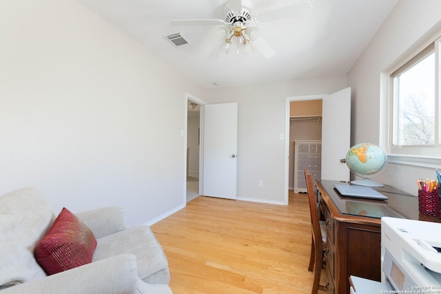 home office featuring visible vents, baseboards, light wood-type flooring, and a ceiling fan