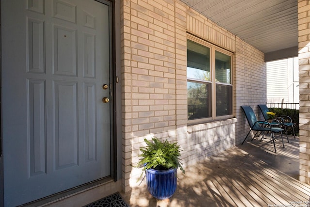 view of exterior entry featuring brick siding and covered porch