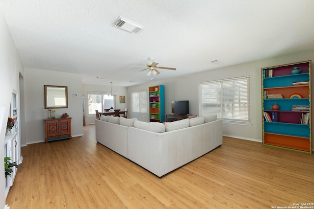 living area with baseboards, visible vents, light wood finished floors, ceiling fan, and a textured ceiling