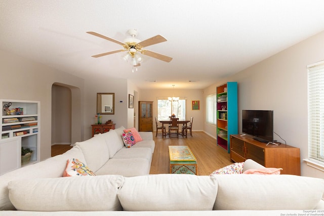 living area featuring light wood-type flooring, arched walkways, and ceiling fan with notable chandelier