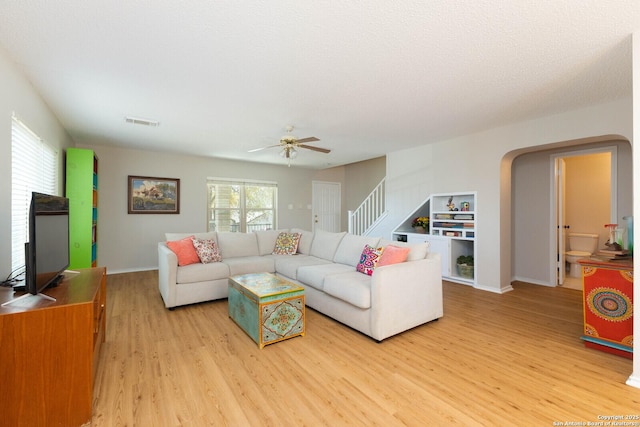 living room with visible vents, baseboards, stairway, light wood-style floors, and a ceiling fan