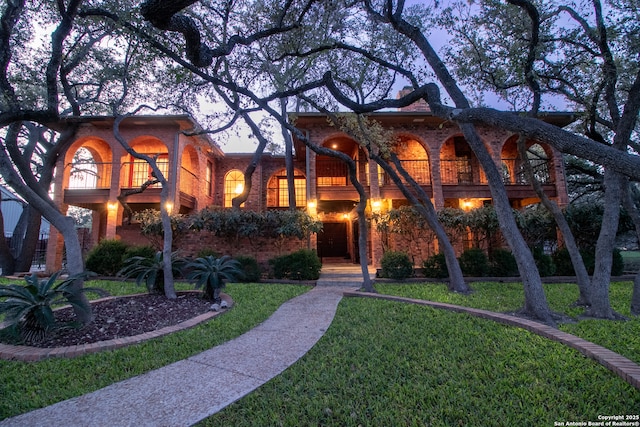 view of front facade with brick siding, a balcony, and a front yard