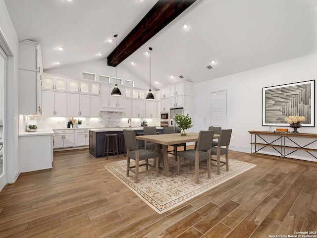 dining area with baseboards, visible vents, high vaulted ceiling, light wood-style floors, and beamed ceiling