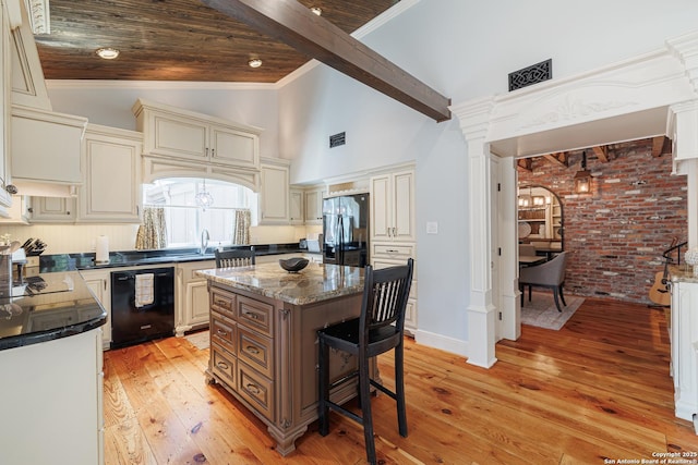 kitchen featuring cream cabinetry, black appliances, light wood-style flooring, a breakfast bar, and dark stone countertops